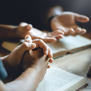 Christian group of people holding hands praying worship to believe and Bible on a wooden table for devotional or prayer meeting concept.